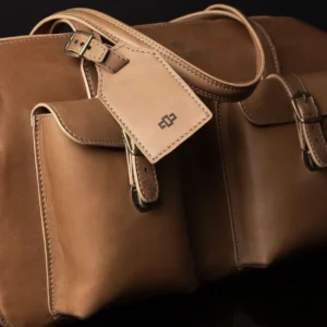 Closeup view of Marcella Overnight Duffle Bag in tan leather, showcasing it's luggage tag and exterior pockets.