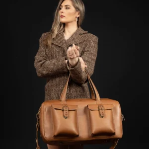 Women’s Marcella Overnight Duffle Bag in tan leather, held by model, showcasing its structured design and refined craftsmanship.