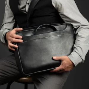 Seated model holding the Astin Sleek black leather laptop bag, emphasizing its compact and sophisticated design.