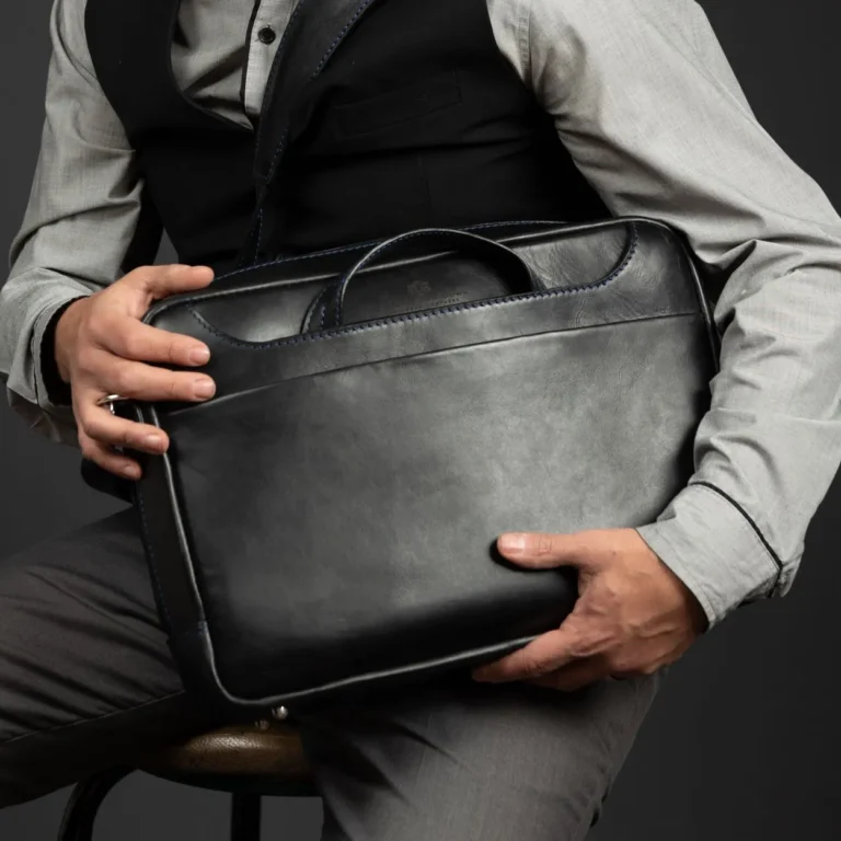 Seated model holding the Astin Sleek black leather laptop bag, emphasizing its compact and sophisticated design.