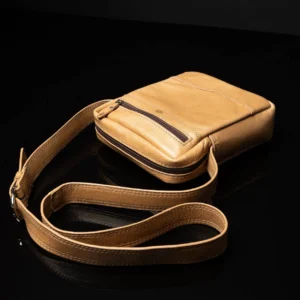 Montrose Sling Bag in tan full-grain leather, neatly coiled to display its adjustable strap and premium craftsmanship.