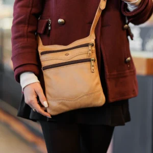 Woman carrying the Dakota Sling Bag in tan, showcasing its slim design, adjustable strap, and elegant full-grain leather.