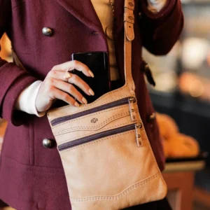Close-up of a woman holding the Dakota Sling Bag in tan, highlighting its stylish, compact design and premium leather finish.