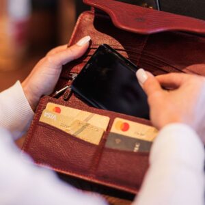 Close-up of a woman using the ruby red Genevieve leather smart phone purse, demonstrating the spacious compartments and secure magnetic closure.