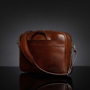 Angled view of Astin Sleek polished brown leather laptop bag, highlighting its tucked handles and reinforced stitching.
