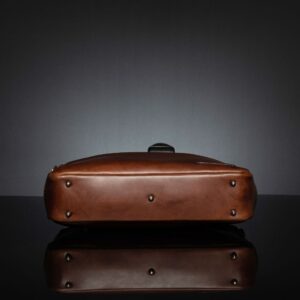 Bottom view of Astin Sleek polished brown leather laptop bag, featuring a sturdy base with protective metal feet for stability.