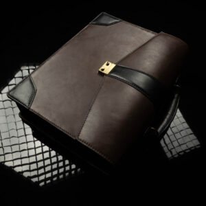 Angled artistic shot of the Svelte Laptop Bag, showcasing its brown leather body, black trims, and sleek, structured design while laying flat.