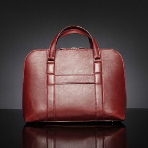 Back view of women's Reagan Euro ruby red leather laptop bag, equipped with a luggage strap for easy travel use.