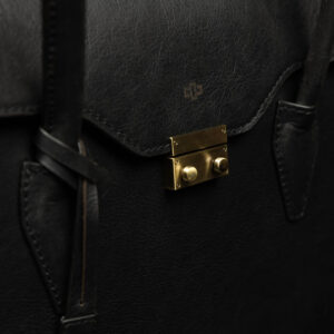 Close-up of gold-tone lock on women's black leather laptop tote bag, highlighting elegant security feature.