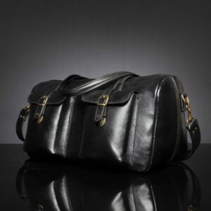 Angled view of Marcella Overnight Duffle Bag in black leather, showcasing it's shape and 2 front pockets.