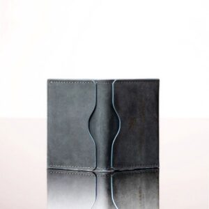 Close-up of denim blue leather, smooth texture, and curved stitching detail on a compact bifold wallet.